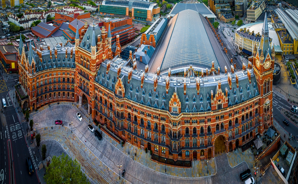Aerial view of St Pancras Renaissance Hotel and St Pancras International railway station in London, featuring Victorian Gothic architecture with ornate brickwork and a large arched glass roof over the station.
