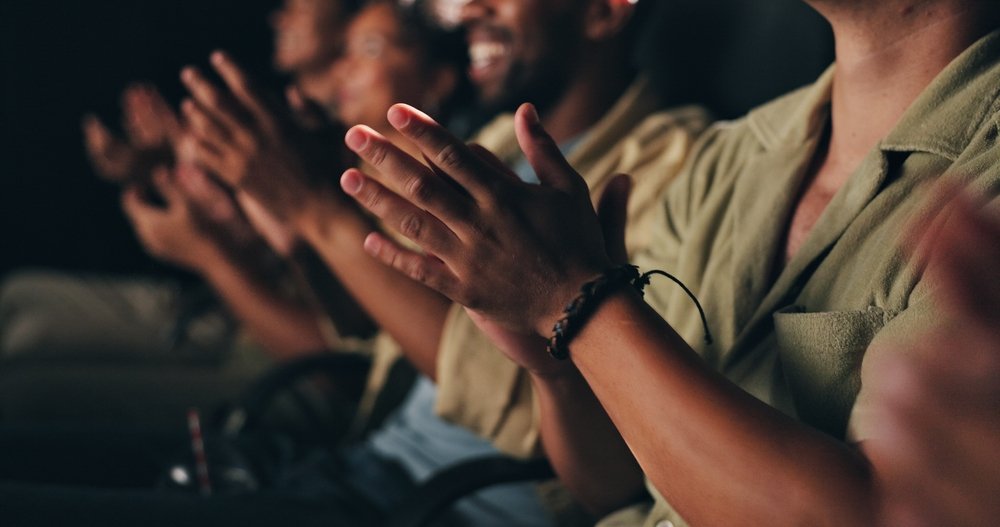 A row of people seated in an audience, clapping enthusiastically with smiles on their faces—perhaps celebrating a fantastic performance after visiting one of the Best Places to Eat Near Covent Garden Before a Theatre Show.