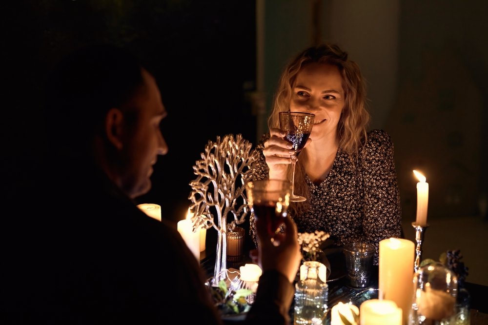 A woman and a man sit at a candlelit table, smiling and making a toast with wine glasses. The woman faces the camera, enjoying one of the Best Places to Eat Near Covent Garden Before a Theatre Show, with candles and a small metallic tree ornament on the table.