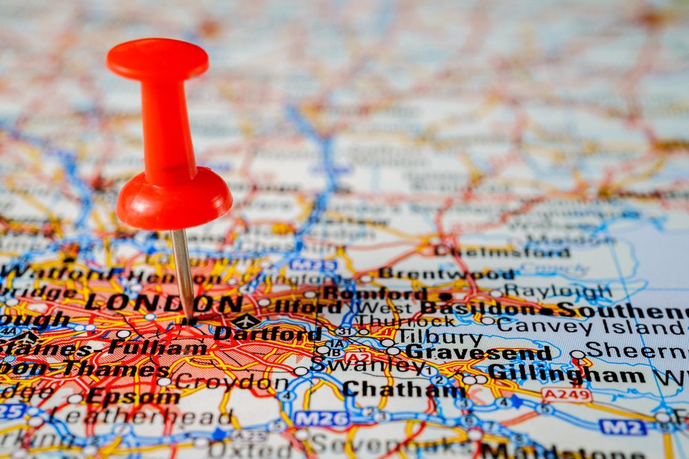 A red pushpin is placed on a detailed map, marking the city of London and its surrounding areas in southern England. The map shows roads, towns, and cities with colorful lines and labels.