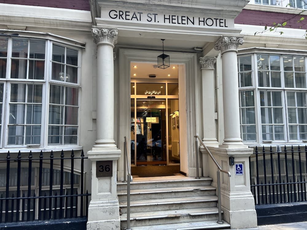 Entrance to the Great St. Helen Hotel, featuring white columns, steps with a railing, a wheelchair access sign, and large windows on either side of the doorway. The building's street number, 36, is visible.