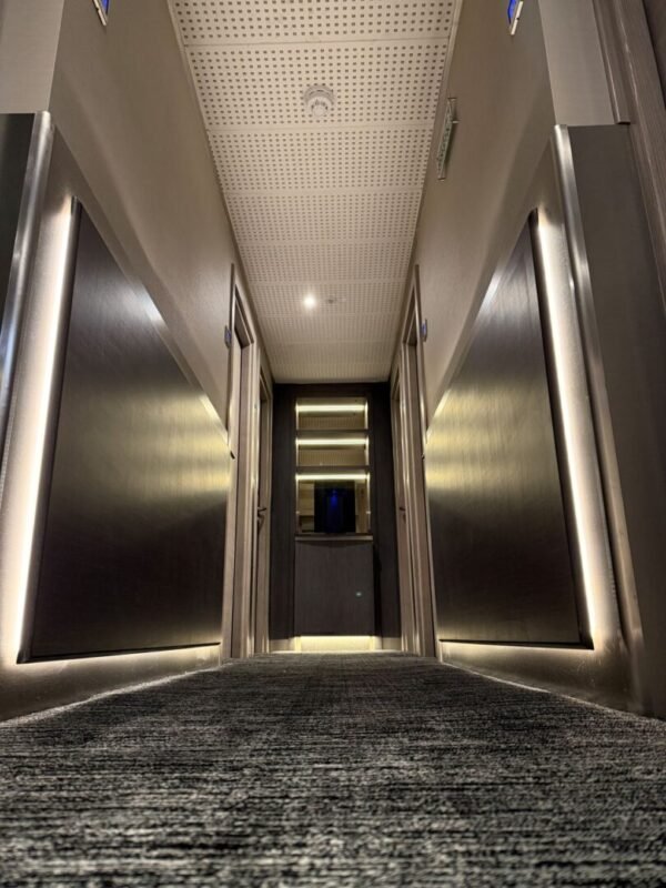 A low-angle view of a modern hotel hallway with carpeted floors, metallic wall panels, and soft ambient lighting along the walls, leading to a closed door at the end—an inviting scene often found in hotels near Kings Cross such as the renowned Mabledon Court Hotel and other stylish hotels in WC1H.