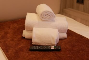 A neatly stacked arrangement of white towels sits on a brown surface, with a TV remote control placed in front of them—a welcoming touch often found in hotels in WC1H such as the Mabledon Court Hotel.