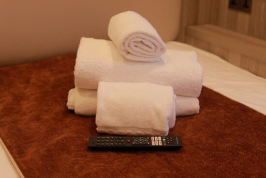 A neatly stacked arrangement of white towels sits on a brown surface, with a TV remote control placed in front of them—a welcoming touch often found in hotels in WC1H such as the Mabledon Court Hotel.